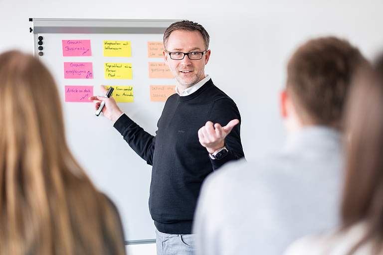 Workshop-Situation: Björn erklärt Inhalte am Whiteboard mit Haftnotizen und diskutiert mit Teilnehmern.