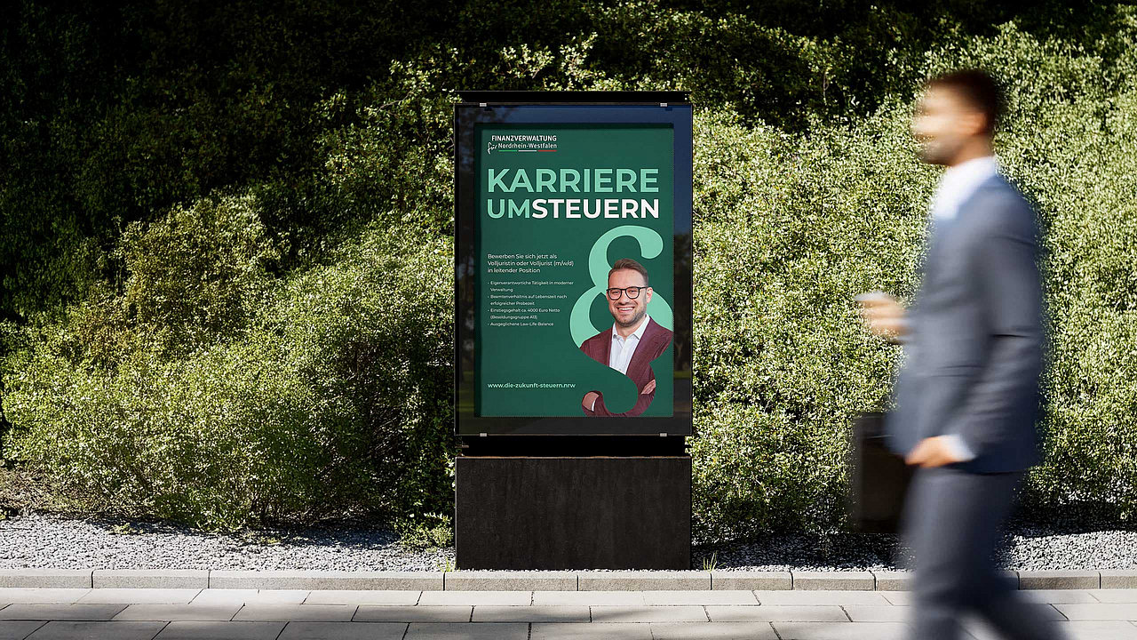 Citylight der Finanzverwaltung NRW mit dem Slogan "Karriere umsteuern" und einem lächelnden Mann mit Brille, der eine Volljuristen-Stelle bewirbt.
