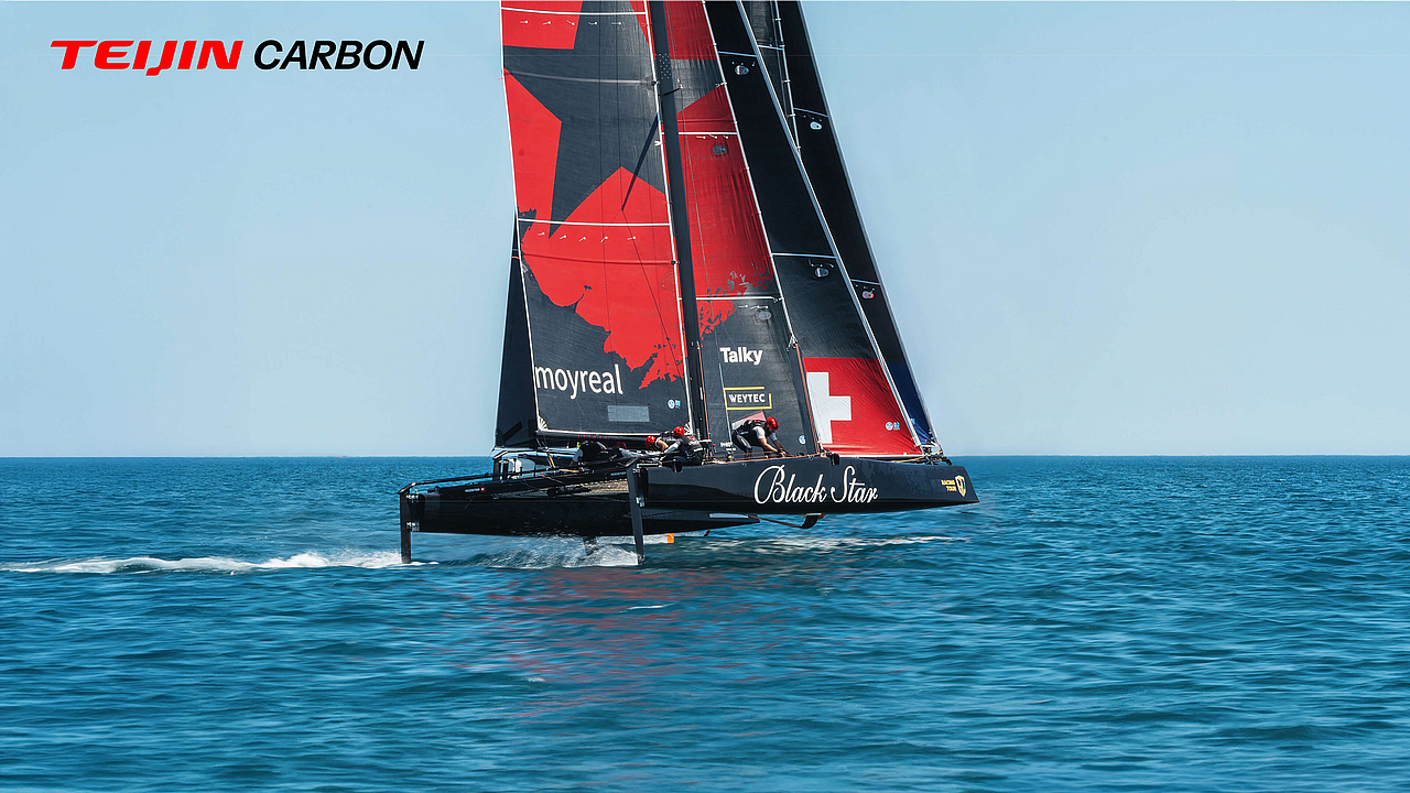 Ein Black Star GC32 Segelkatamaran mit rotem und schwarzem Segel in voller Fahrt auf dem Wasser, mit Teijin Carbon Logo.