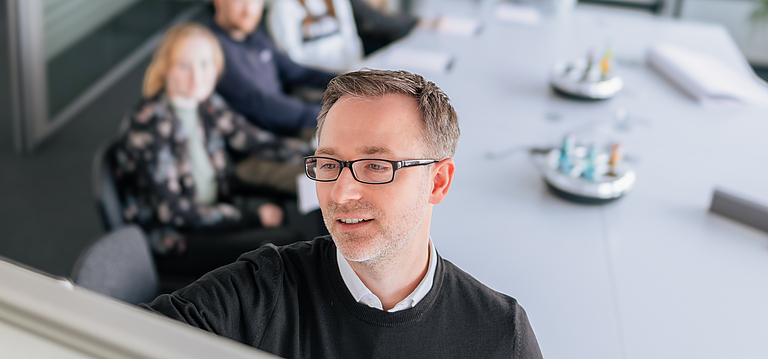 Björn präsentiert Inhalte an einem Flipchart während eines Strategieworkshops, im Hintergrund sitzt ein Team an einem Konferenztisch und hört aufmerksamzu.