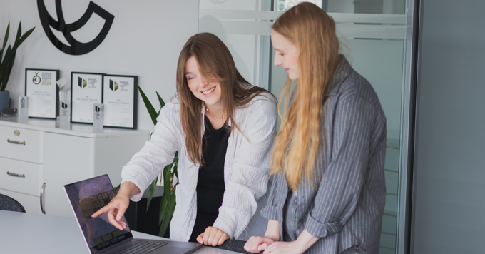Zwei Mitarbeiterinnen besprechen gemeinsam Inhalte einer B2B Kampagne auf einem Laptop während eines Meetings in einem modernen Büro.