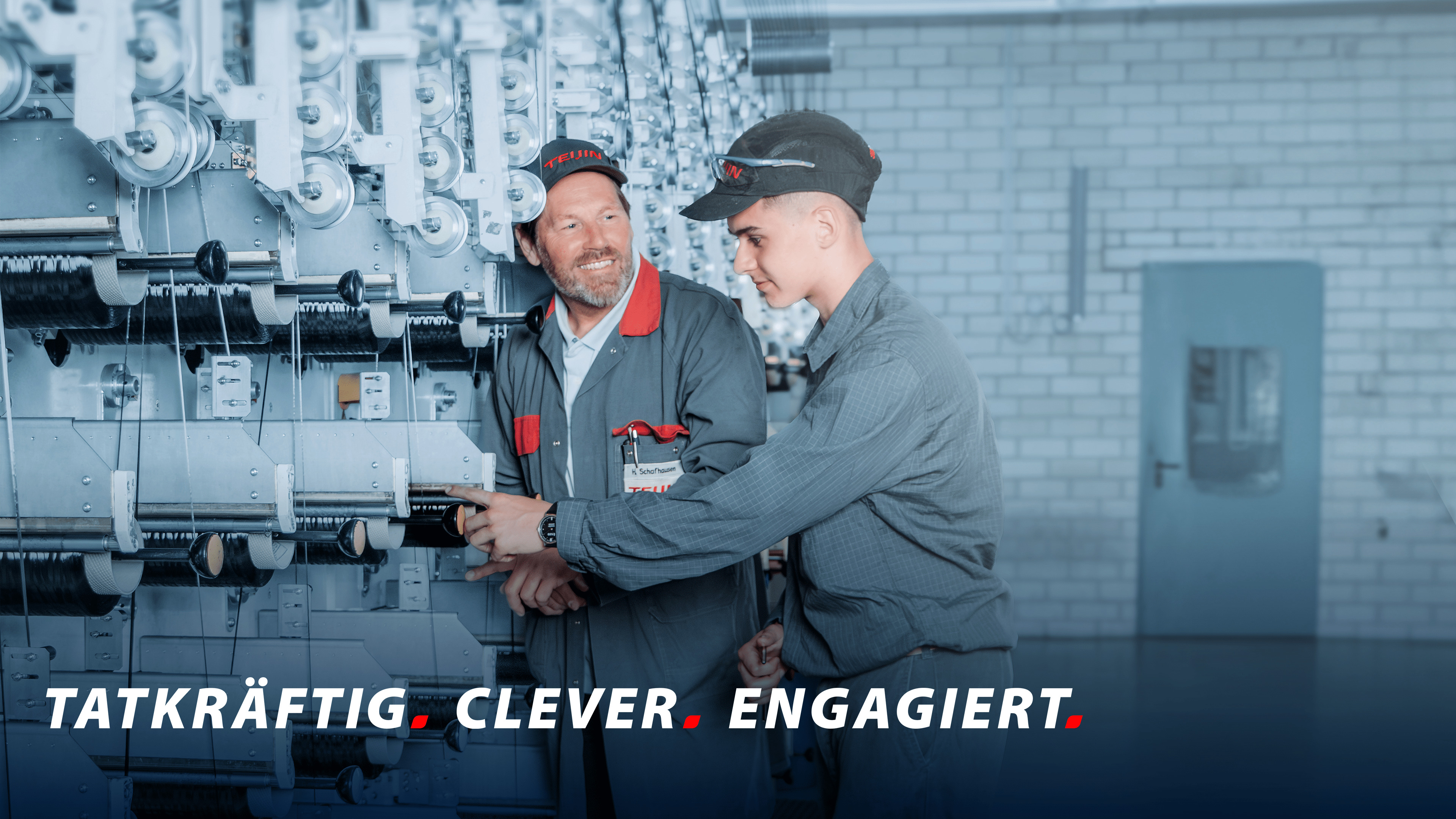 Ein erfahrener und ein junger Mitarbeiter von Teijin Carbon bei der Arbeit an einer technischen Maschine in einer Industriehalle.